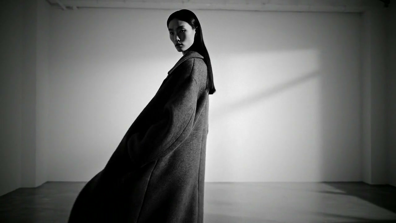 A model in a wool coat in a bright studio, in black and white with deep contrast